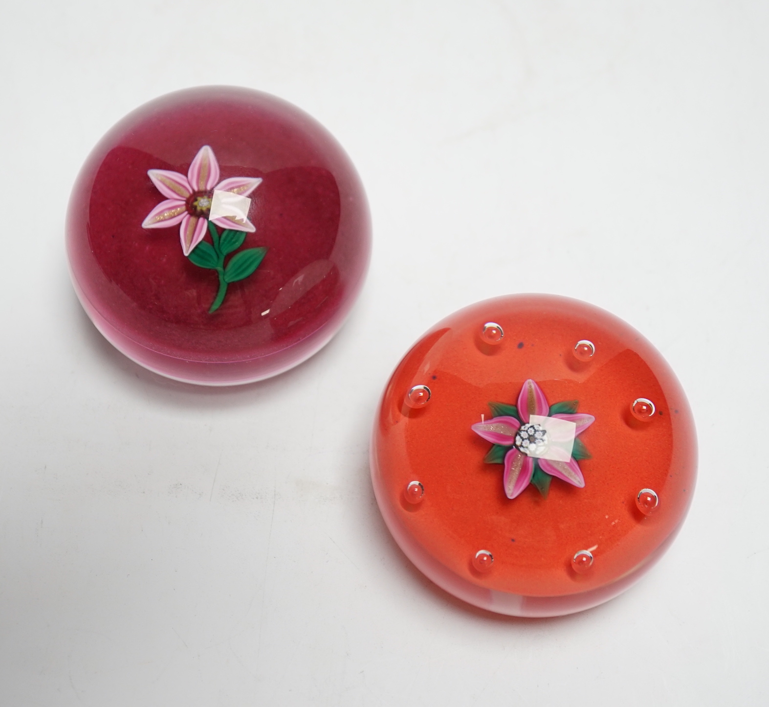 Two Paul Ysart glass ‘flower specimen’ paperweights, both Harland period, the first with a pink and aventurine flower with green stem on a raspberry ground, H cane to base, PY label, 7cm, The second with a pink and adven